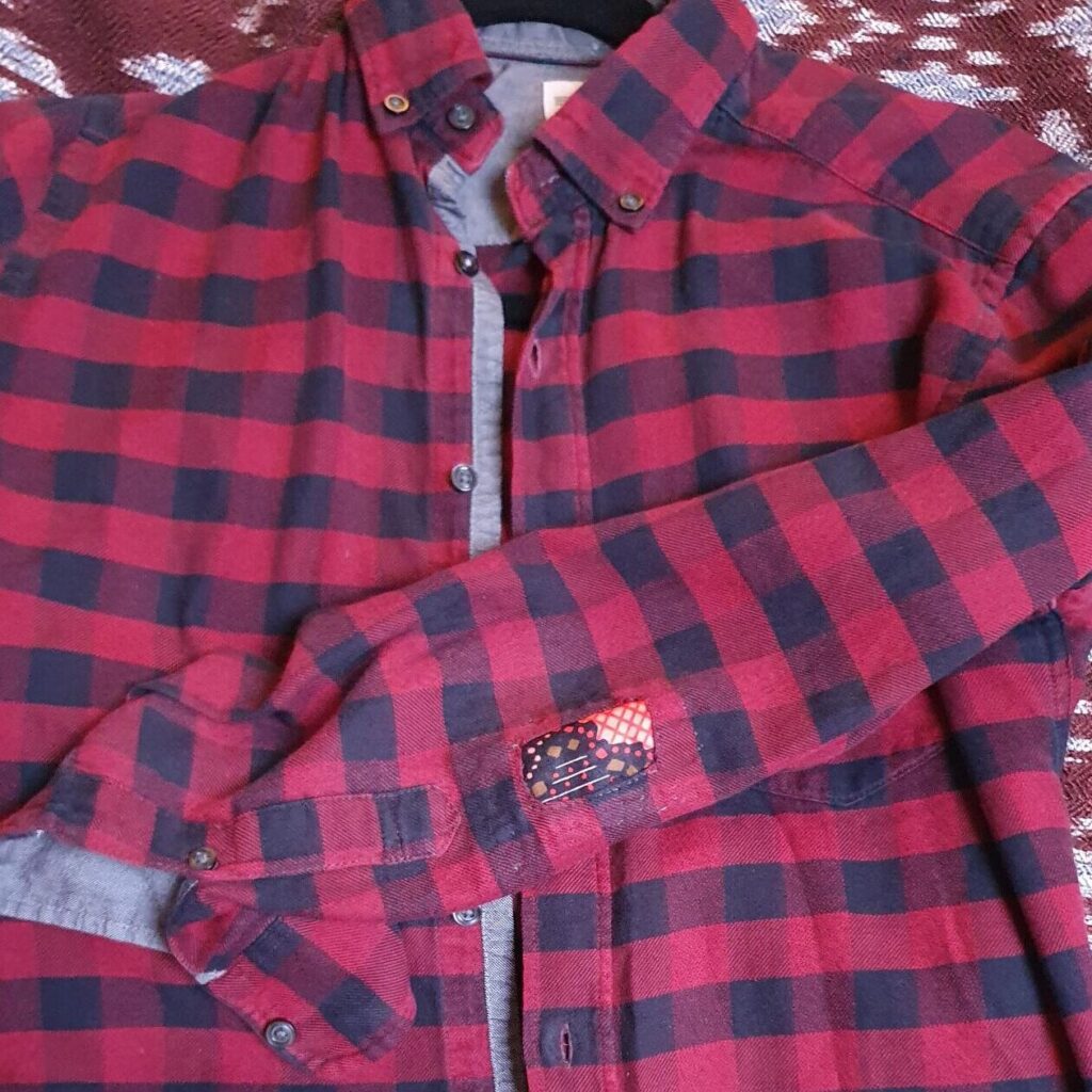 Red plaid shirt mended with visible patch on elbow
