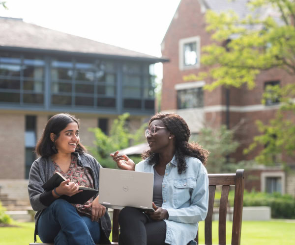 Two students sit on a bench, discussing something animatedly.